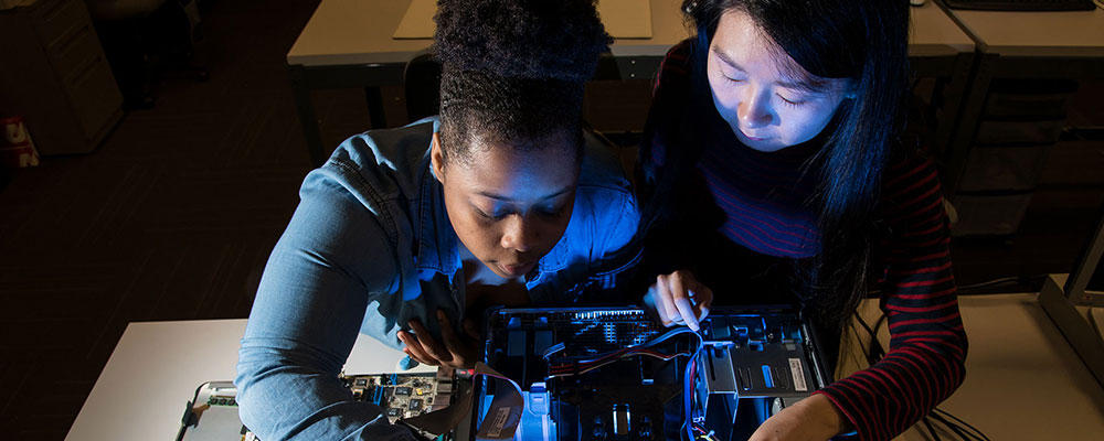 Two female college students examining computer case interior.